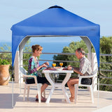 Two people sitting at a table under a blue pop-up canopy on a deck with ocean view.