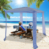 Two people sitting under a striped canopy on a sandy beach with palm trees and blue sky.