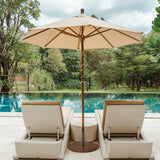 Beige patio umbrella and lounge chairs by a pool with greenery in the background