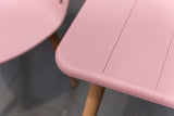 Close-up of a pink table with wooden legs on a gray floor.
