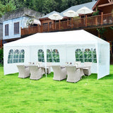 White outdoor canopy tent with tables and chairs on a grassy area, with a building in the background.