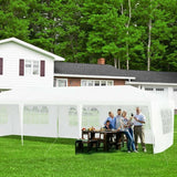 Family gathered around a table under a white outdoor canopy in a backyard setting with trees and a house in the background.