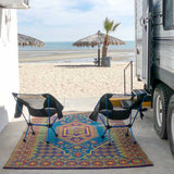 Two camping chairs on a colorful Turkish Aqua rug in front of an RV by a beach.