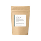 Kraft paper packaging with a label for 'Of the Sea' bath salts on a white background