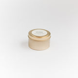 Small cream-colored candle in a tin with a gold lid on a light gray background Orange + Clove