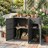 A dark gray wicker-style outdoor storage cabinet with two doors open, styled on a brick patio in a garden with potted plants and gardening tools inside and on top.