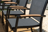 Row of outdoor chairs with black mesh seats and brown armrests on a gravel surface.