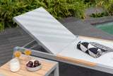 White lounge chair with wooden armrests by a poolside, featuring a small table with drinks and fruit.