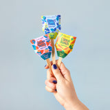 Hand holding three colorful seed pop packages against a light blue background
