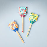 Three wooden spatulas with colorful packaging on a gray background Seed Pops - Pollinator