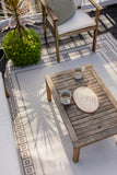Wooden outdoor table with coffee cups and a coaster on a patio with a patterned Border White Sand Outdoor Rug