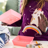 Person wearing a purple shirt with a cartoon design, holding pink trays.