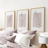 Three framed abstract line art prints on a wall above a bed with pillows and bedding.