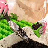 Person planting seeds in a container with gardening tools and gloves.