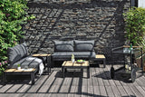 Outdoor patio set with gray cushions on a wooden deck against a stone wall.