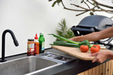 Person preparing vegetables on a cutting board by a sink with a grill in the background