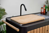 Outdoor kitchen setup with a black sink and wooden cutting board.