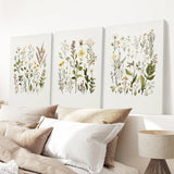 Three botanical wall art prints above a bed with pillows and a lamp.