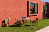 Outdoor seating area with wooden table and chairs against a red wall.