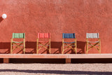 Four colorful director's chairs lined up against a red wall.
