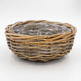 A round woven wicker basket with a natural brown and beige textured weave, shown on a clean white background with a clear plastic liner inside.