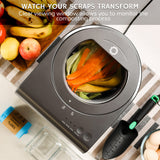 Composting device with clear viewing window showing food scraps, surrounded by fruits and a garden tool.
