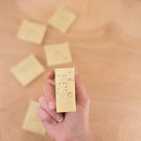 Hand holding a bar of soap with specks on a wooden surface