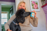Woman holding a black dog and a bottle of ROSEMARY MINT EXFOLIATING BODY WASH 16 oz. (with Arnica & Epsom Salt)
