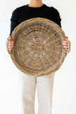 Person holding a large round wicker basket against a white background