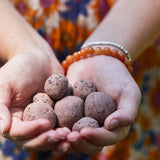 Hands holding small brown Seed Bombs with a colorful patterned fabric background