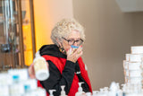 Person wearing glasses and a red jacket in a room with stacks of bottles.