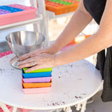 Colorful 5X5 Shallow Microgreen Trays on a table with a person's hands interacting with them.