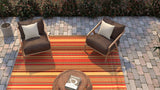 Two brown chairs with white cushions on a red and orange Stripes Warm Brown rug in an outdoor setting.