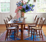 Dining room with wooden table and chairs, colorful flowers, and a Turkish Blue rug.