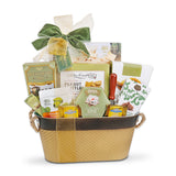 A gourmet gift basket filled with assorted cheeses, crackers, and snacks, tied with a green and cream bow. Visible items include Brie cheese, a peanut butter bottle, and other packaged food products arranged inside a woven basket.