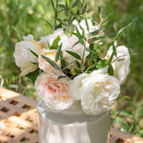 Bouquet of white Top Cream Roses with green leaves on a white pedestal against a blurred natural background.