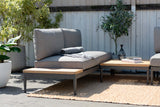 Outdoor patio set with gray cushions and wooden coffee table on a stone patio.