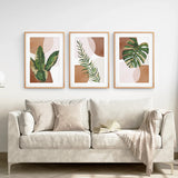 Beige sofa with decorative pillows and a blanket, featuring three framed3 Piece Terracotta Boho Wall Art. Green Tropical Leaves on the wall.