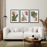 Modern living room with a white sofa, round wooden coffee table, and three framed 3 Piece Terracotta Boho Wall Art. Green Tropical Leaves on the wall.