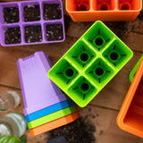 Colorful seedling trays on a wooden surface with soil.