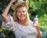 Woman outdoors wearing a cowboy hat and holding a bottle of VANILLA GOATS MILK LOTION