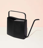 Black watering can on a light pink background