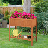 Wooden garden planter with pink flowers and gardening tools on a grassy area.