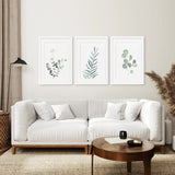 Modern living room with a white sofa, wooden coffee table, and Watercolor Botanical Set of 3 Prints Wall Decor featuring green leaves.