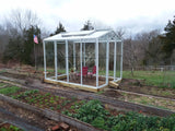 Janco Greenhouse in a garden with raised beds and trees in the background