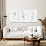 Modern living room with a white sofa, wooden coffee table, and floral line art prints on the wall.