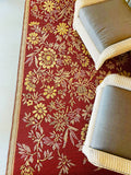 Floral-patterned Wildflowers Cranberry red rug with wicker chairs and cushions on a white floor.