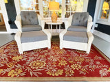 White wicker chairs with gray cushions on a red floral Wildflowers Cranberry rug in a sunroom.