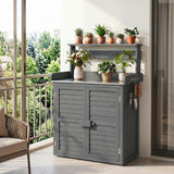 A gray outdoor utility cabinet with a top shelf and hanging tools, styled on a balcony with potted plants and a window view of green trees.