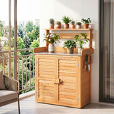 A light natural wood outdoor storage cabinet with a slatted double door, a white stone-look top, and an open upper shelf holding several potted plants. The cabinet is shown on a balcony with a tiled floor, a window view, and a chair partially visible.